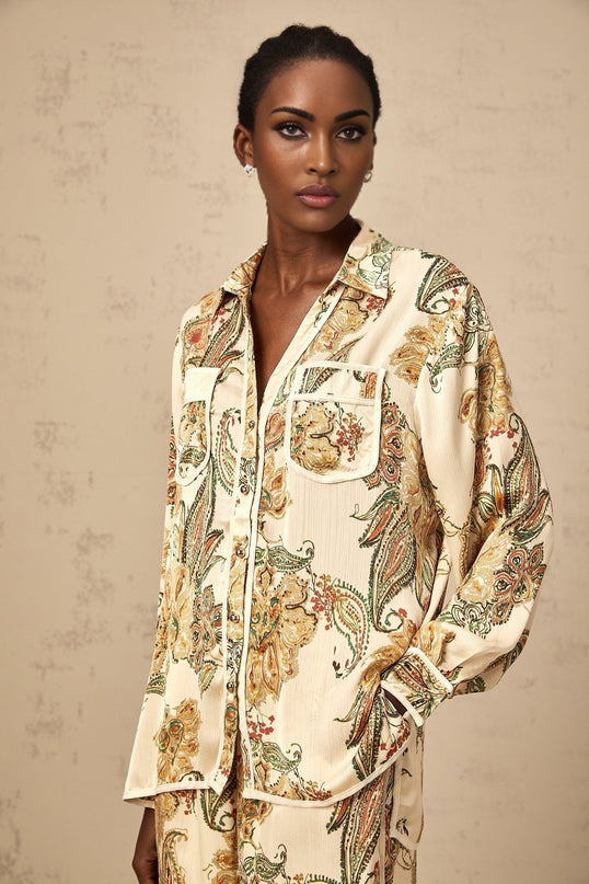 Woman wearing light colored floral print matching shirt and trousers set with neutral tones standing in relaxed pose