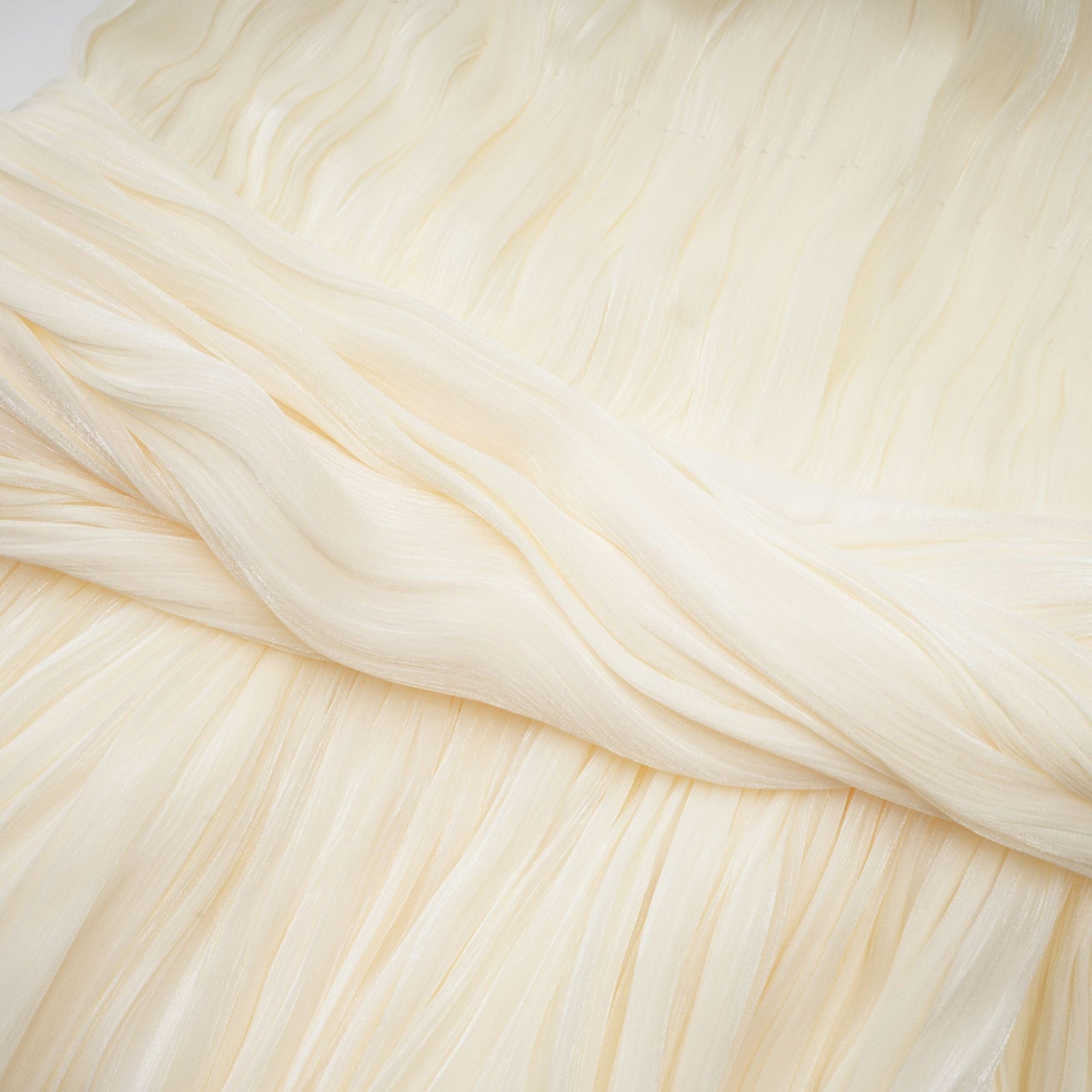 Woman wearing light colored pleated mini dress with ribbon detail at waist standing in relaxed pose