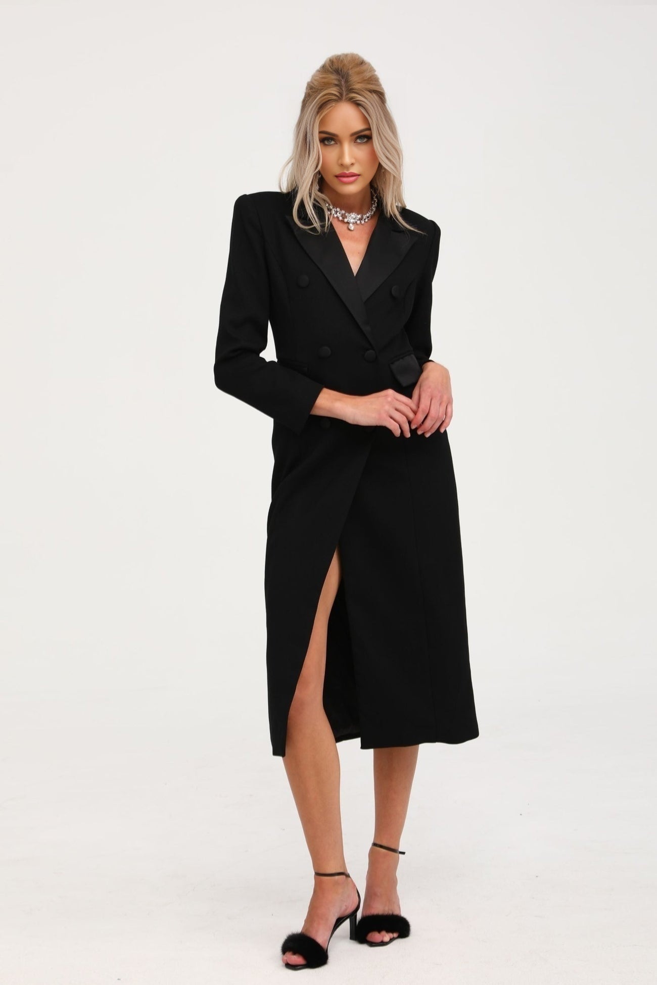 Woman wearing long black double breasted coat named Eithne standing against plain background