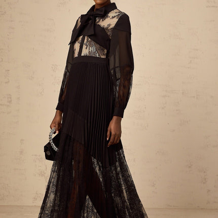 Woman wearing long black dress with floral lace panels and pleated skirt