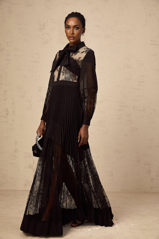 Woman wearing long black dress with floral lace panels and pleated skirt