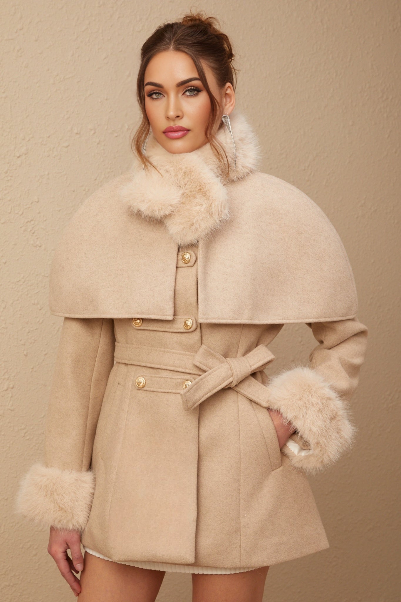 Woman wearing long black faux fur coat with detachable cape collar standing against neutral background