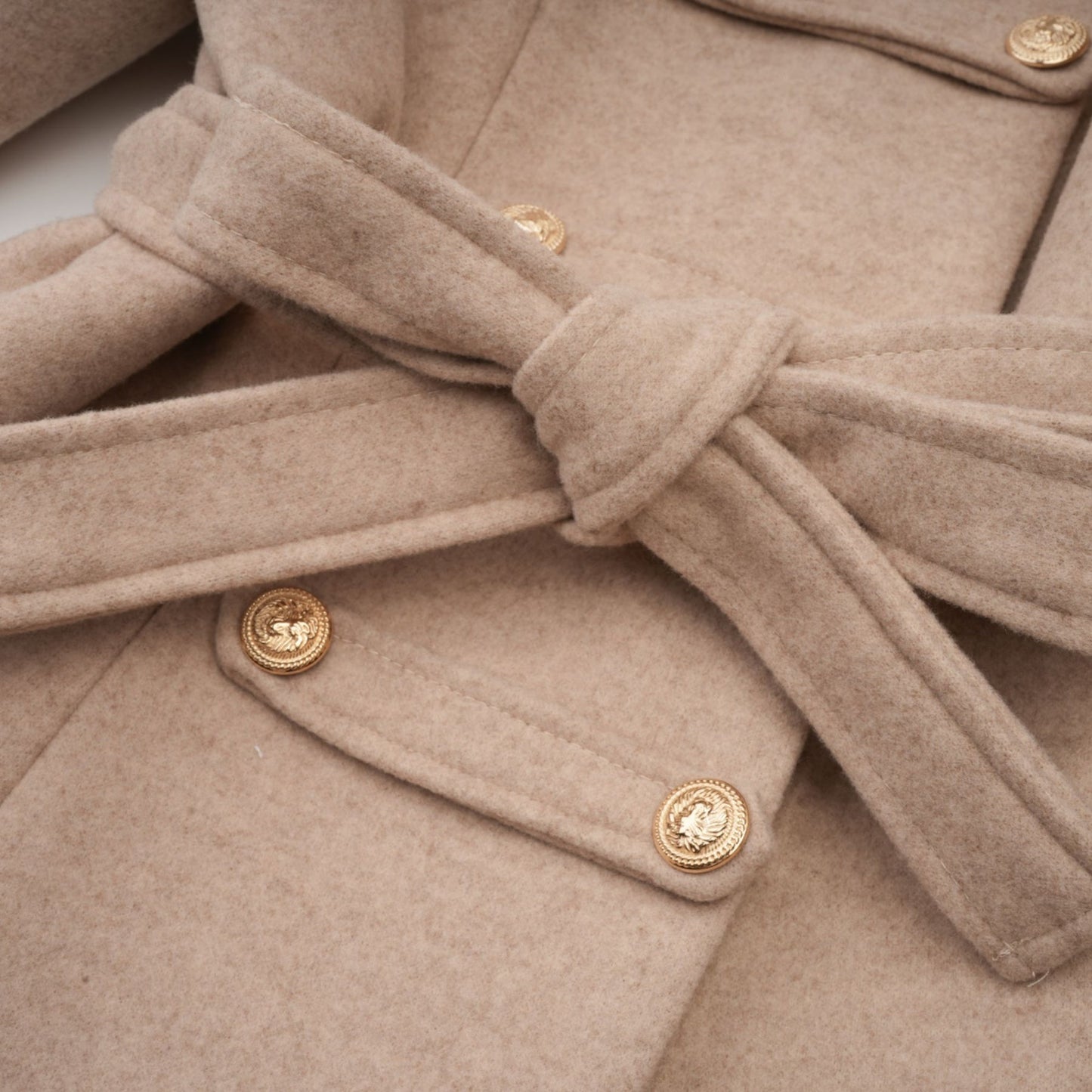Woman wearing long black faux fur coat with detachable cape collar standing against plain background