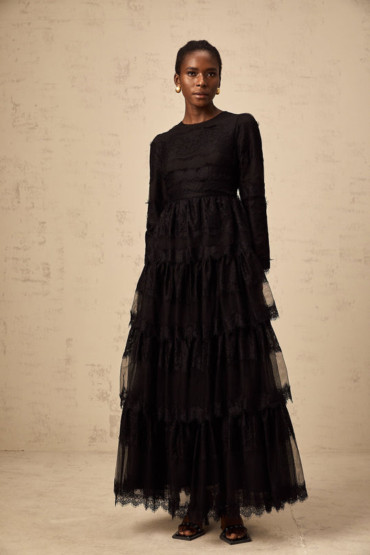 Woman wearing long black lace dress with tiered skirt and sheer tulle details full length view