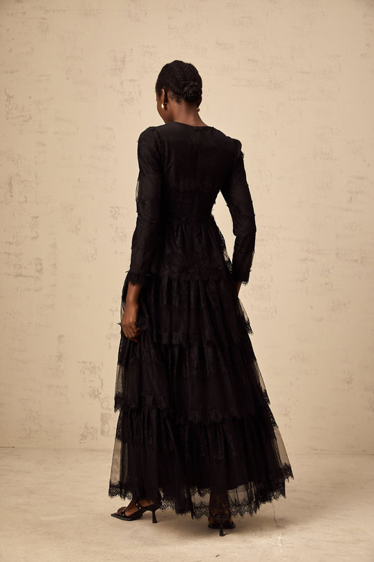 Woman wearing long black lace dress with tiered skirt and sheer tulle details standing in elegant pose