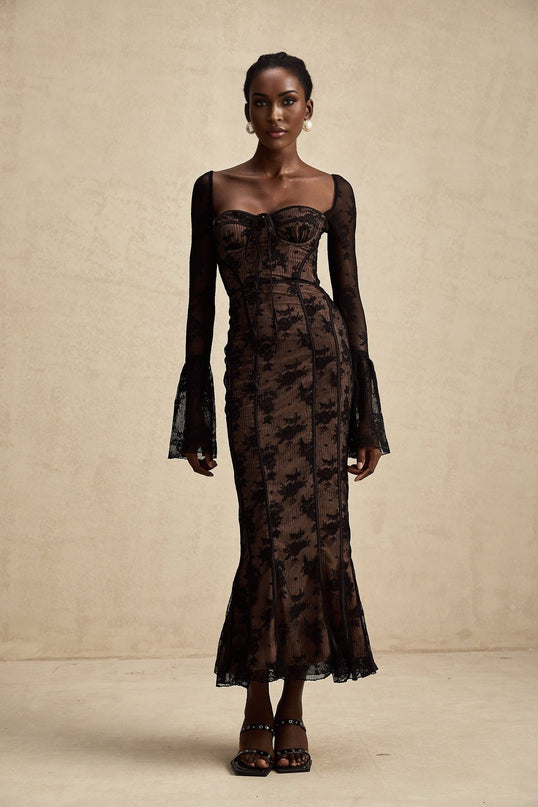 Woman wearing long black lace maxi dress with flared skirt and fitted bodice standing in elegant pose