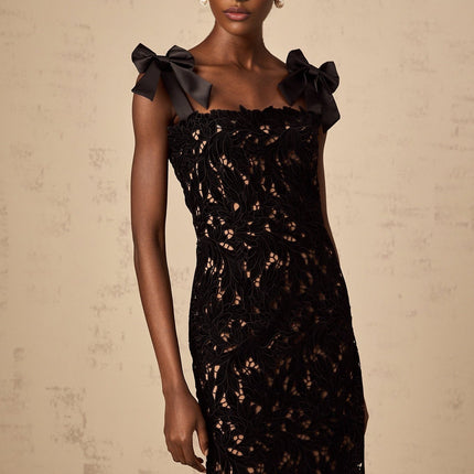 Woman wearing long black maxi dress with floral embroidery details standing against plain background
