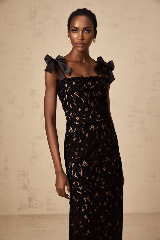Woman wearing long black maxi dress with floral embroidery details standing against plain background