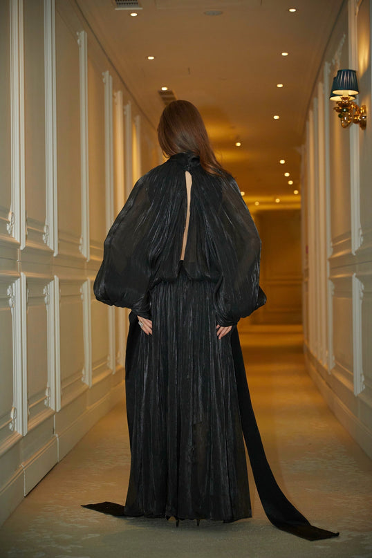 Woman wearing long black pleated satin maxi dress with flowing skirt and fitted bodice