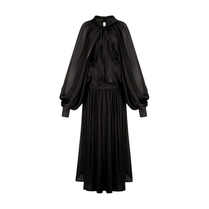Woman wearing long black pleated satin maxi dress with flowing skirt and fitted bodice