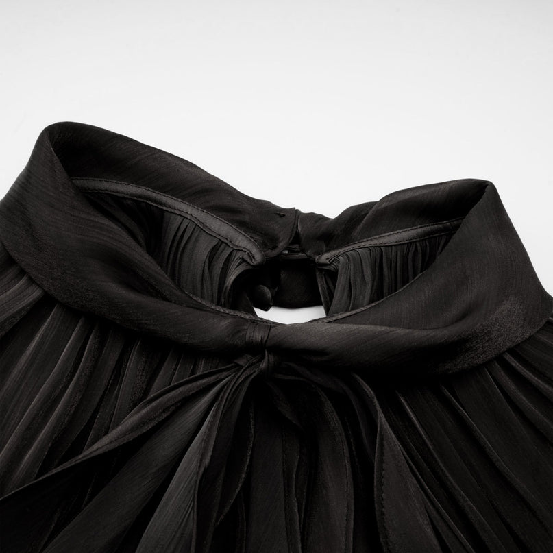Woman wearing long black pleated satin maxi dress with flowing skirt and fitted bodice