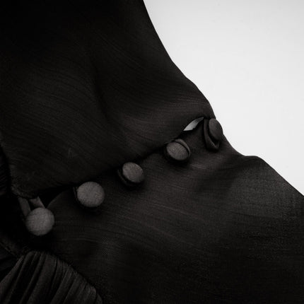 Woman wearing long black pleated satin maxi dress with flowing skirt and fitted bodice