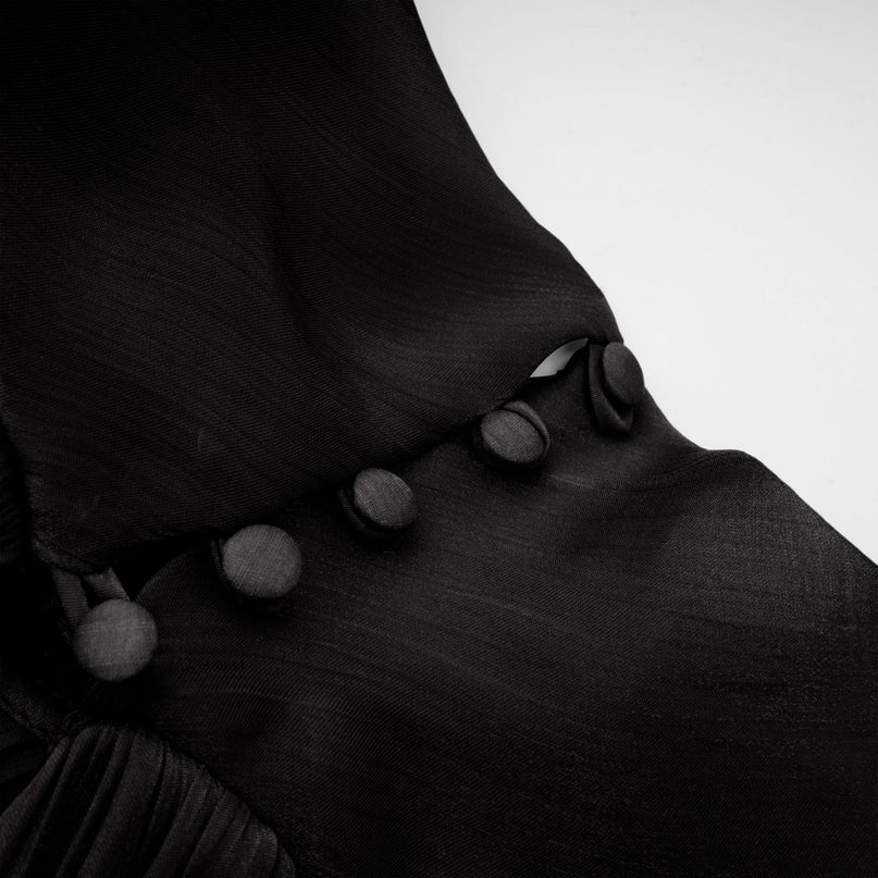 Woman wearing long black pleated satin maxi dress with flowing skirt and fitted bodice