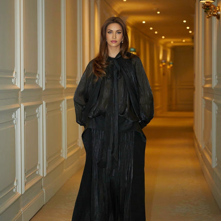 Woman wearing long black pleated satin maxi dress with flowing skirt