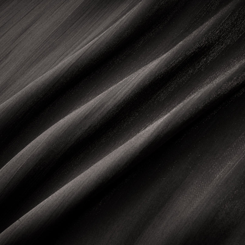 Woman wearing long black pleated satin maxi dress with flowing skirt