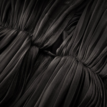 Woman wearing long black pleated satin maxi dress with flowy skirt and fitted bodice