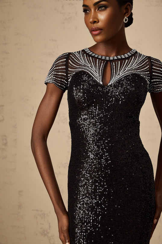 Woman wearing long black sequined maxi dress with cut out details standing against plain background