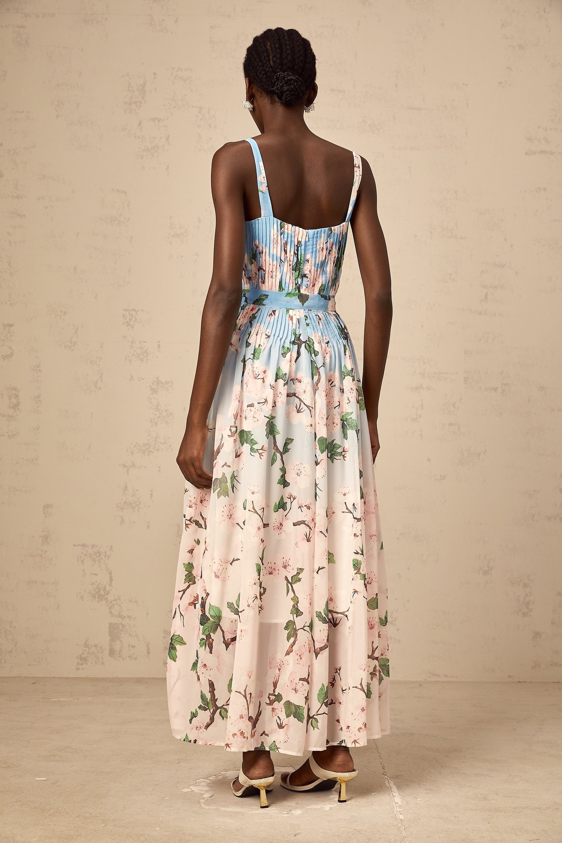 Woman wearing long blue dress with floral print and pleated skirt