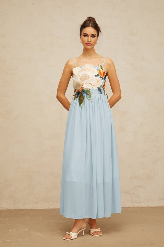 Woman wearing long blue maxi dress with floral embroidery and shirred details