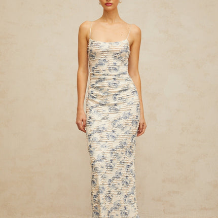 Woman wearing long blue maxi dress with textured floral print pattern and flowing silhouette