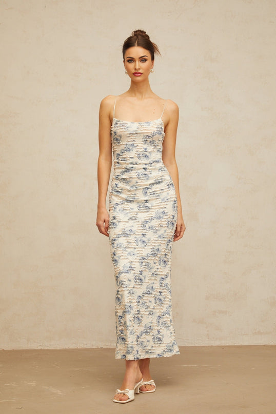 Woman wearing long blue maxi dress with textured floral print pattern and flowing silhouette