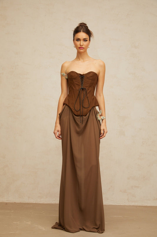 Woman wearing long brown maxi dress with corset bodice and butterfly pin detail