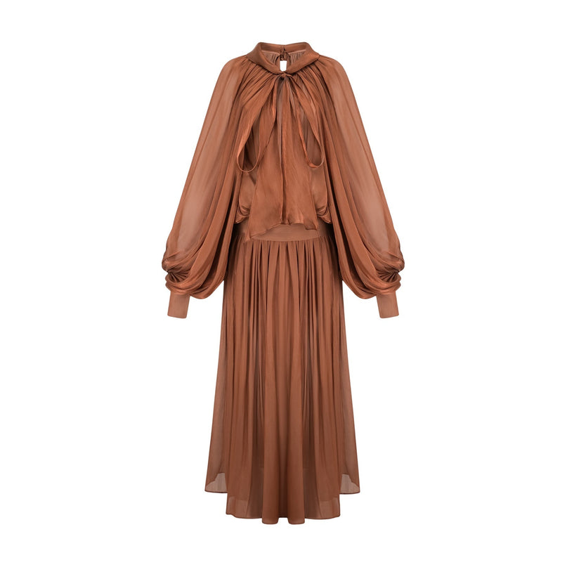 Woman wearing long brown pleated satin maxi dress with flowing skirt and fitted bodice