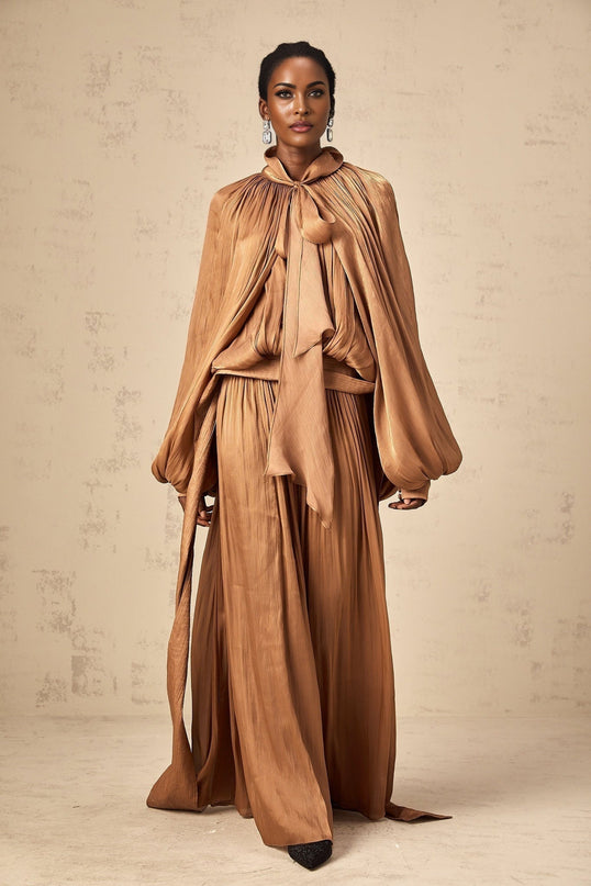 Woman wearing long brown pleated satin maxi dress with flowing skirt and sleeveless design