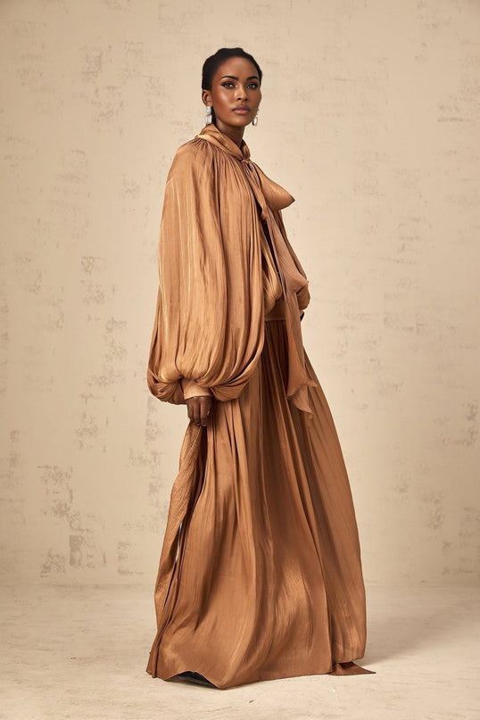 Woman wearing long brown pleated satin maxi dress with flowy skirt and fitted bodice
