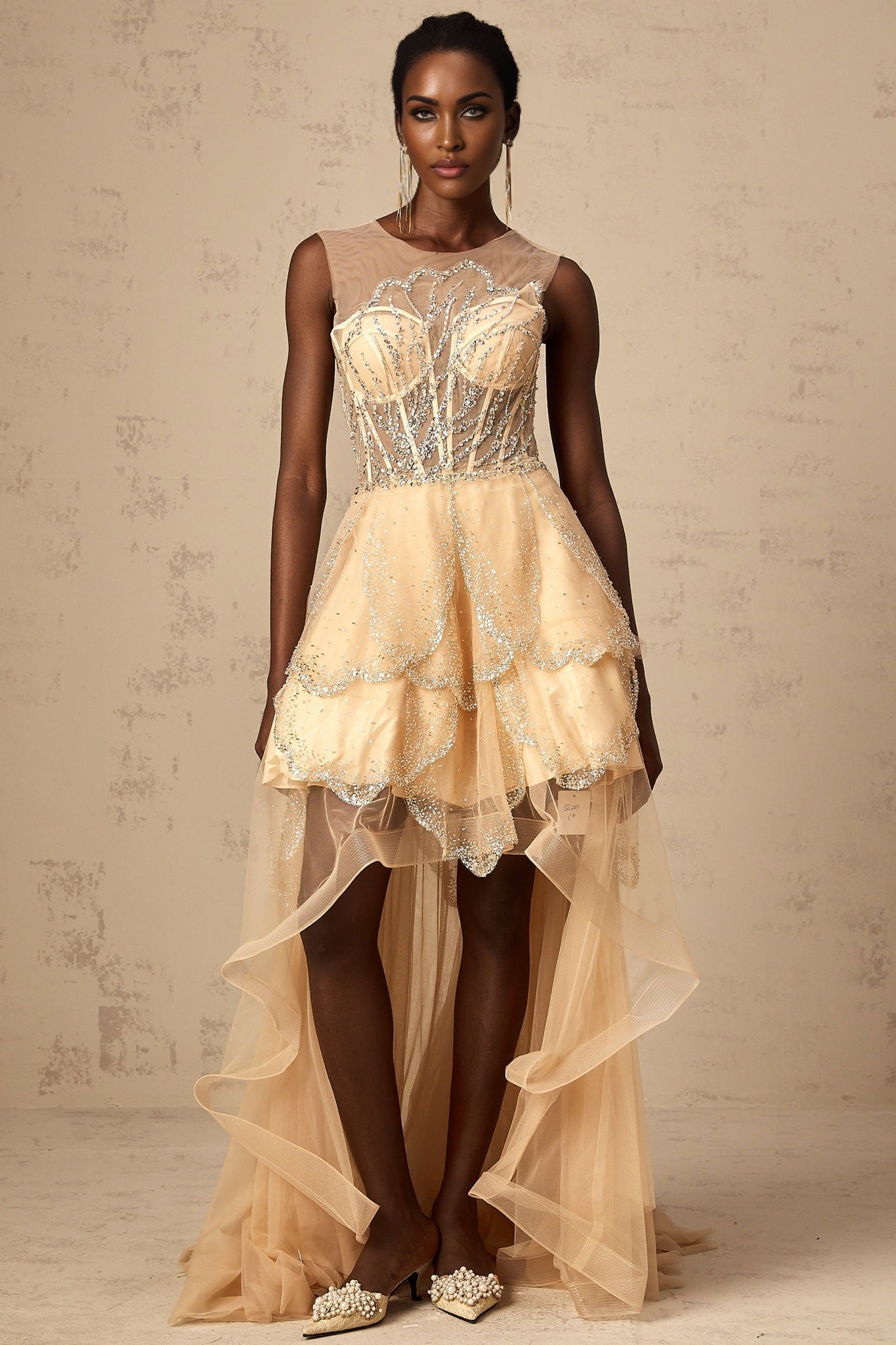 Woman wearing long champagne colored gown with daisy embellishments and high low hemline