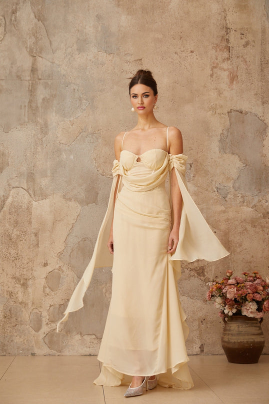 Woman wearing long flowing neutral color chiffon maxi dress with ruched details standing in relaxed pose