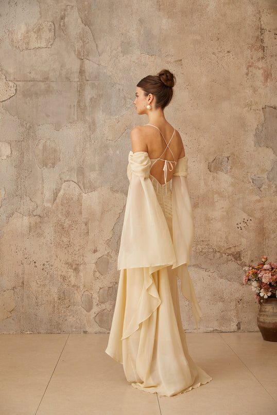 Woman wearing long flowing neutral colored chiffon maxi dress with ruched detailing