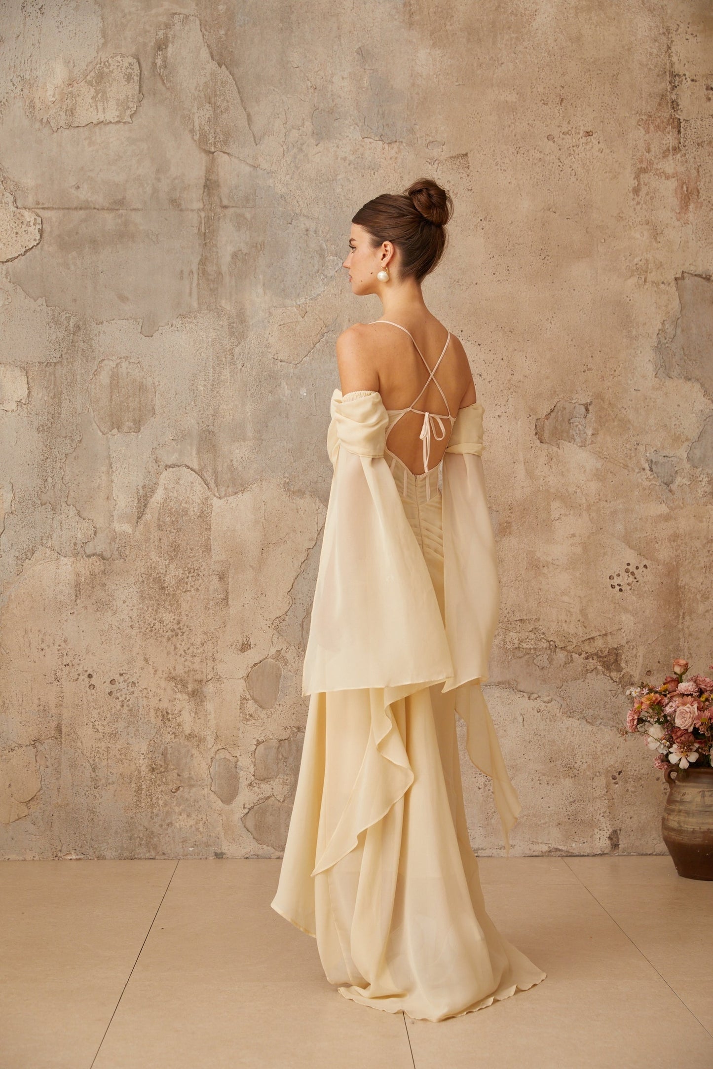 Woman wearing long flowing neutral colored chiffon maxi dress with ruched detailing