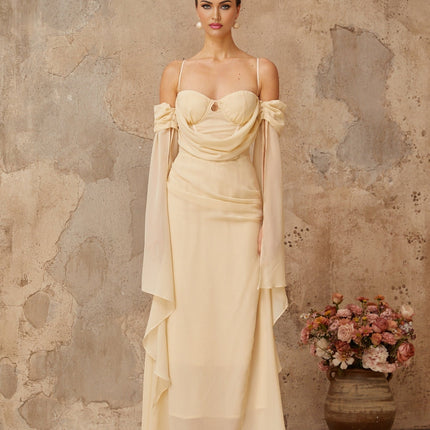 Woman wearing long flowing neutral colored chiffon maxi dress with ruched detailing
