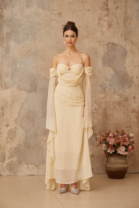 Woman wearing long flowing neutral colored chiffon maxi dress with ruched detailing