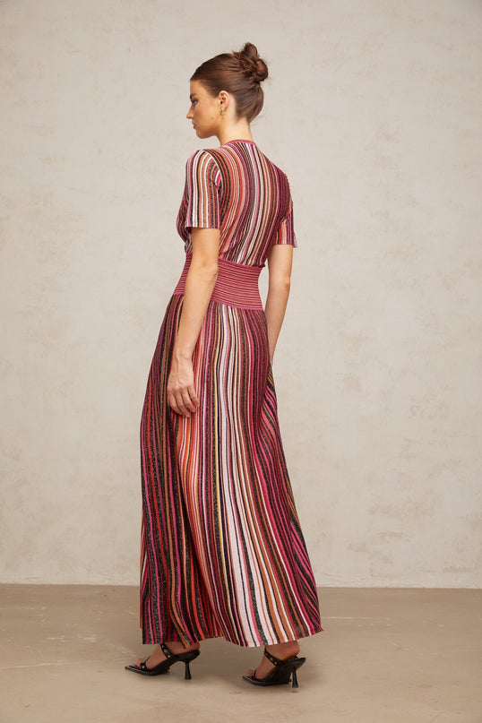 Woman wearing long flowy multicolor metallic knit maxi dress with sleeveless design standing against plain background