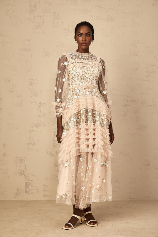 Woman wearing long flowy white maxi dress with colorful floral embroidery and tiered tulle skirt