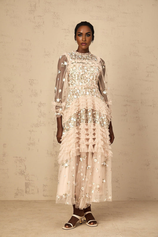 Woman wearing long flowy white maxi dress with colorful floral embroidery and tiered tulle skirt