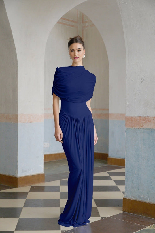 Woman wearing long navy blue asymmetric pleated maxi dress with flowing skirt and sleeveless design