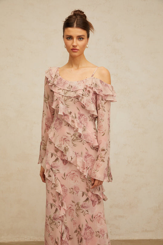 Woman wearing long pink maxi dress with floral print pattern and ruffled details flowing fabric feminine silhouette