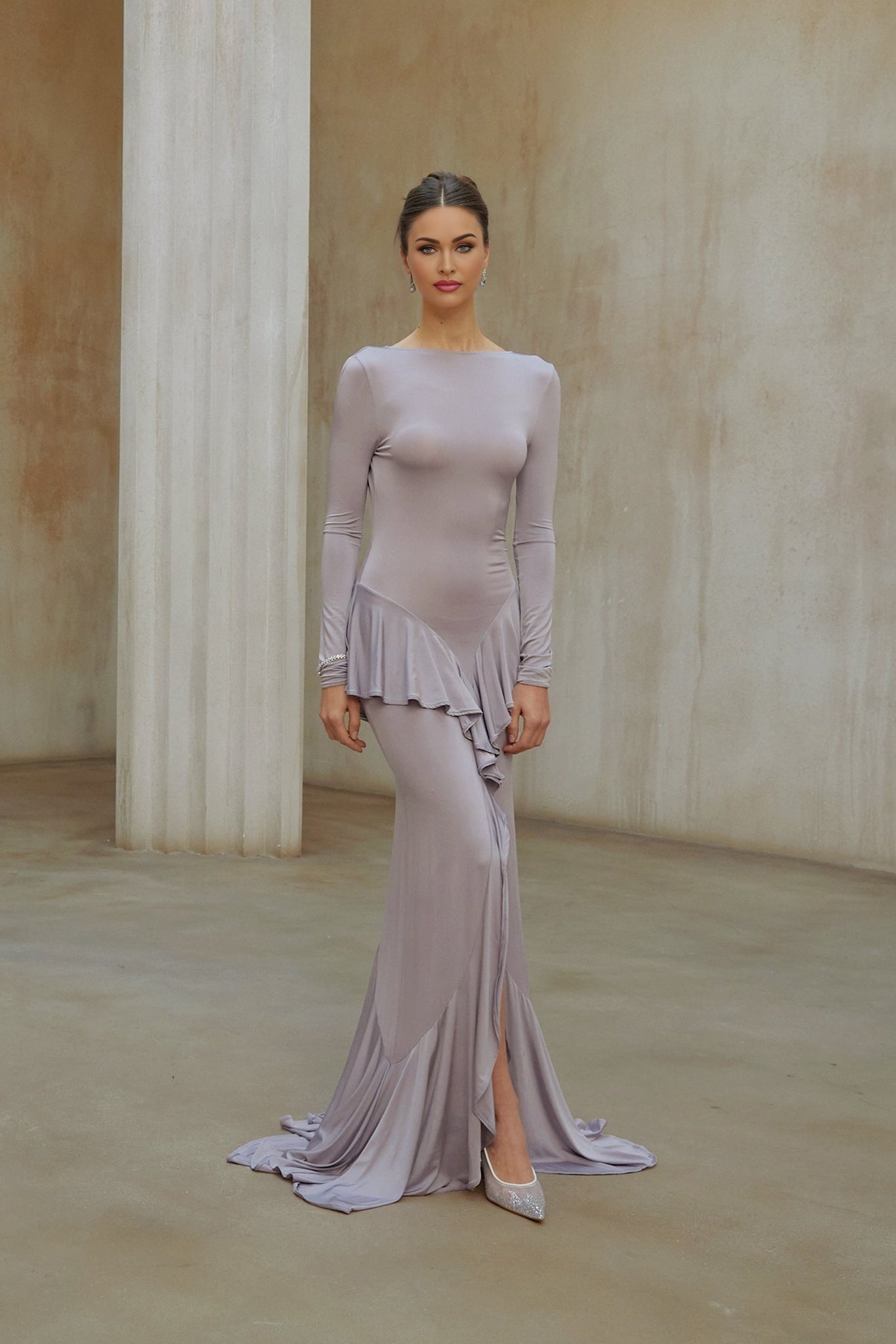 Woman wearing long purple maxi dress with ruffle details and front slit standing against plain background