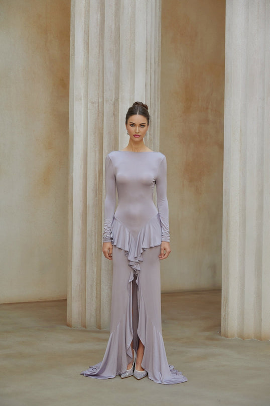 Woman wearing long purple maxi dress with ruffle details and front slit standing in relaxed pose