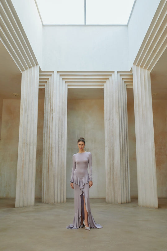 Woman wearing long purple maxi dress with ruffle details and front slit standing in relaxed pose
