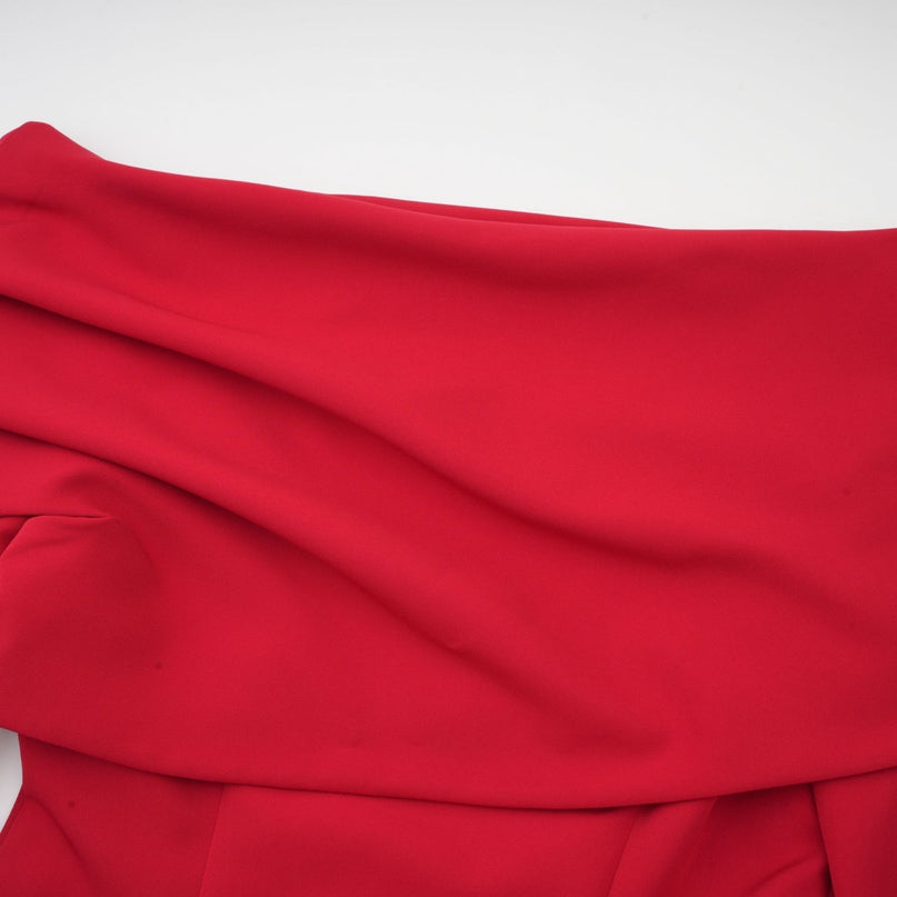 Woman wearing long red pleated maxi dress with high slit standing against plain background