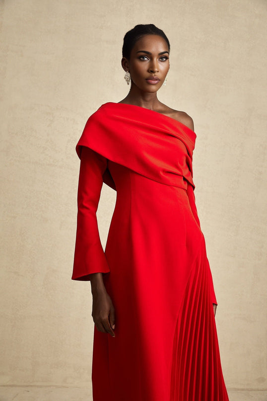 Woman wearing long red pleated maxi dress with high slit standing against plain background