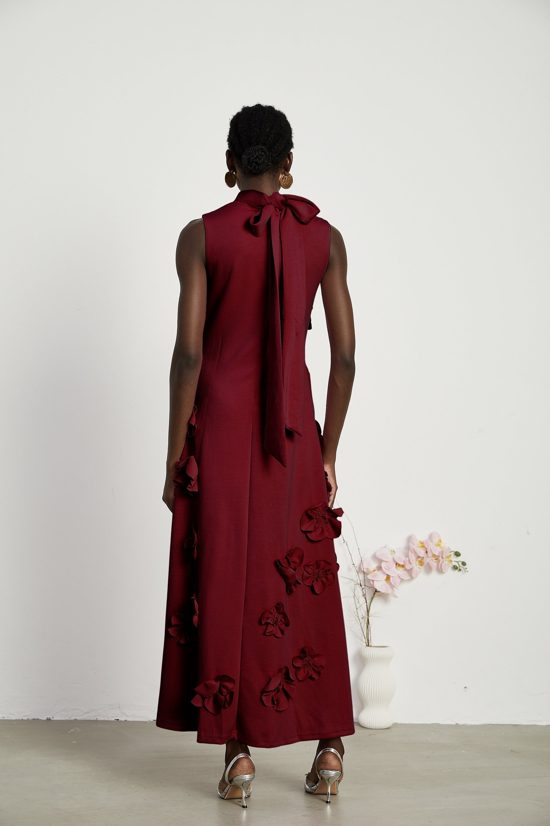 Woman wearing long red sleeveless maxi dress with bow tie detail and faux flower embellishments