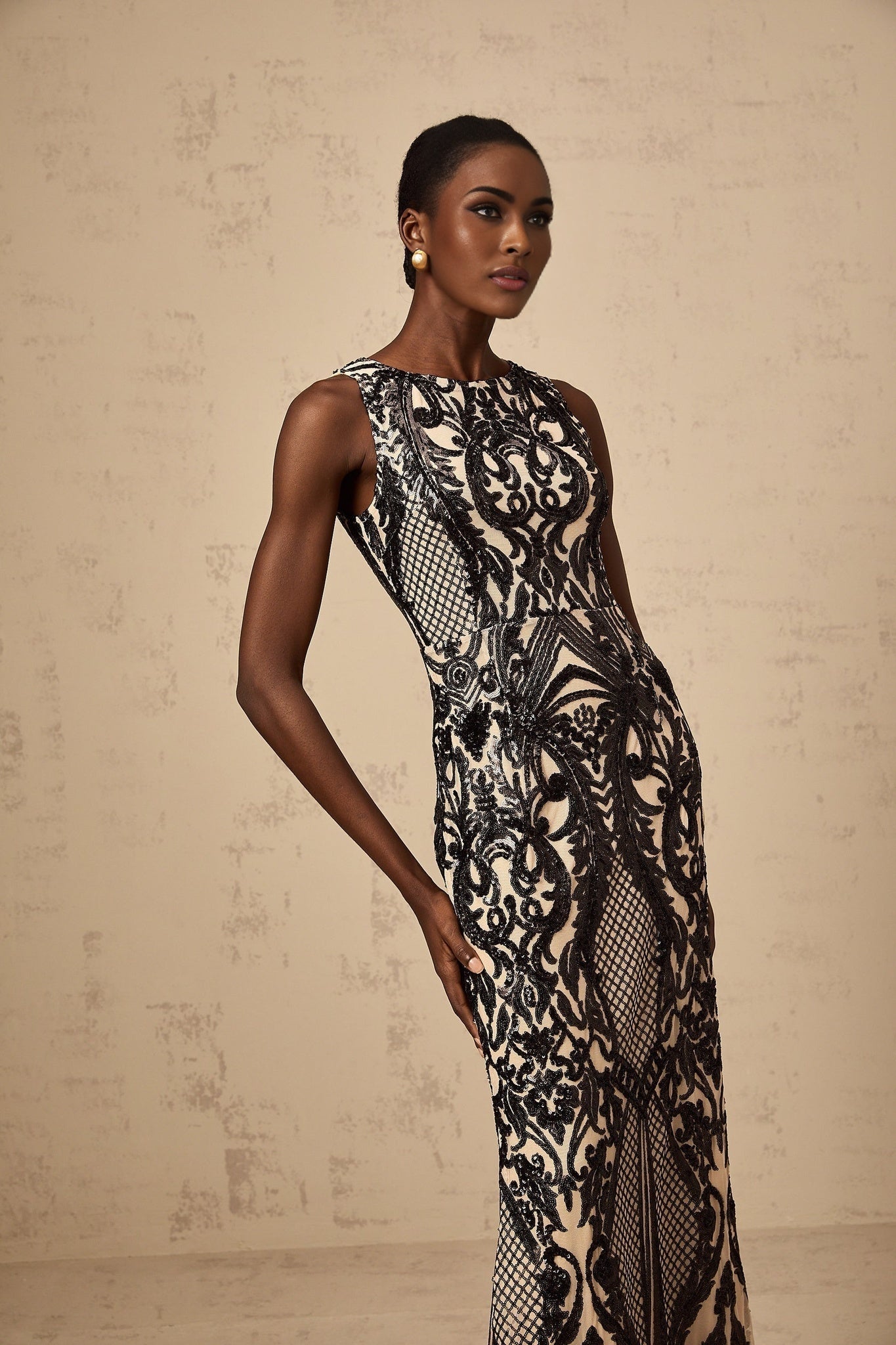 Woman wearing long sequin embellished mesh maxi dress in shimmering gold color with spaghetti straps and flowing skirt