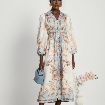 Woman wearing long sleeve floral print boho dress with flowing skirt and v neckline in pastel colors against plain background