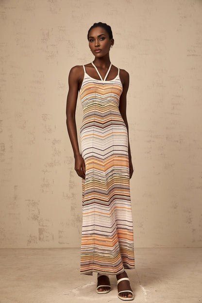 Woman wearing long striped knit maxi dress with multicolored horizontal stripes in pastel shades standing against neutral background