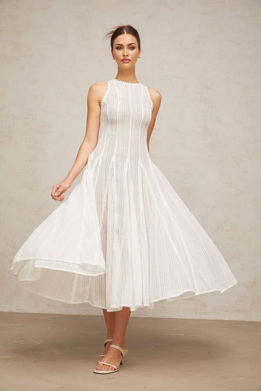 Woman wearing long white dress with puff sleeves and delicate pointelle pattern standing against plain background